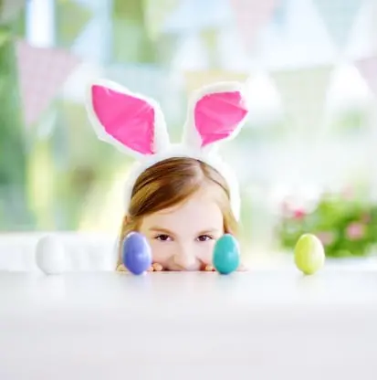 Little girl peering over table at Easter eggs