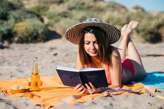 Lady reading book on beach blanket